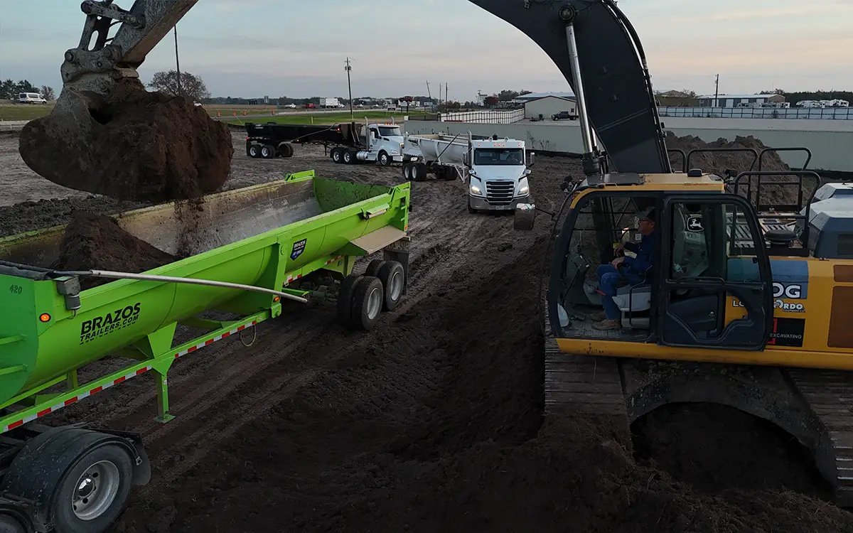 green machine that is in front of a crane getting dirt from it