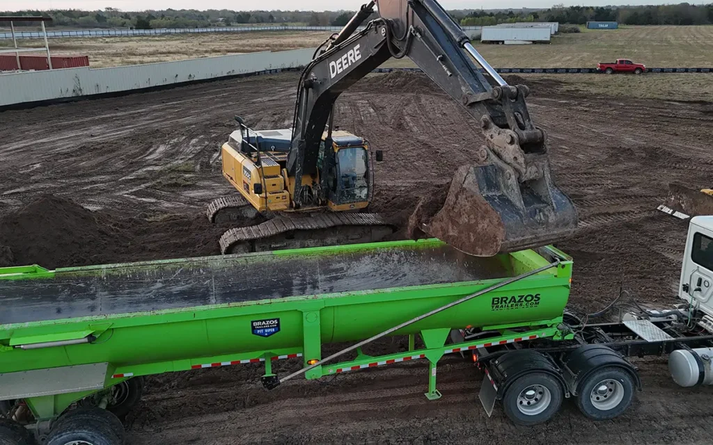 green machine that is in front of a crane getting dirt from it