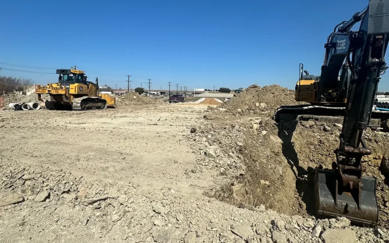 Excavator digging soil while a bulldozer levels dirt at a construction site.